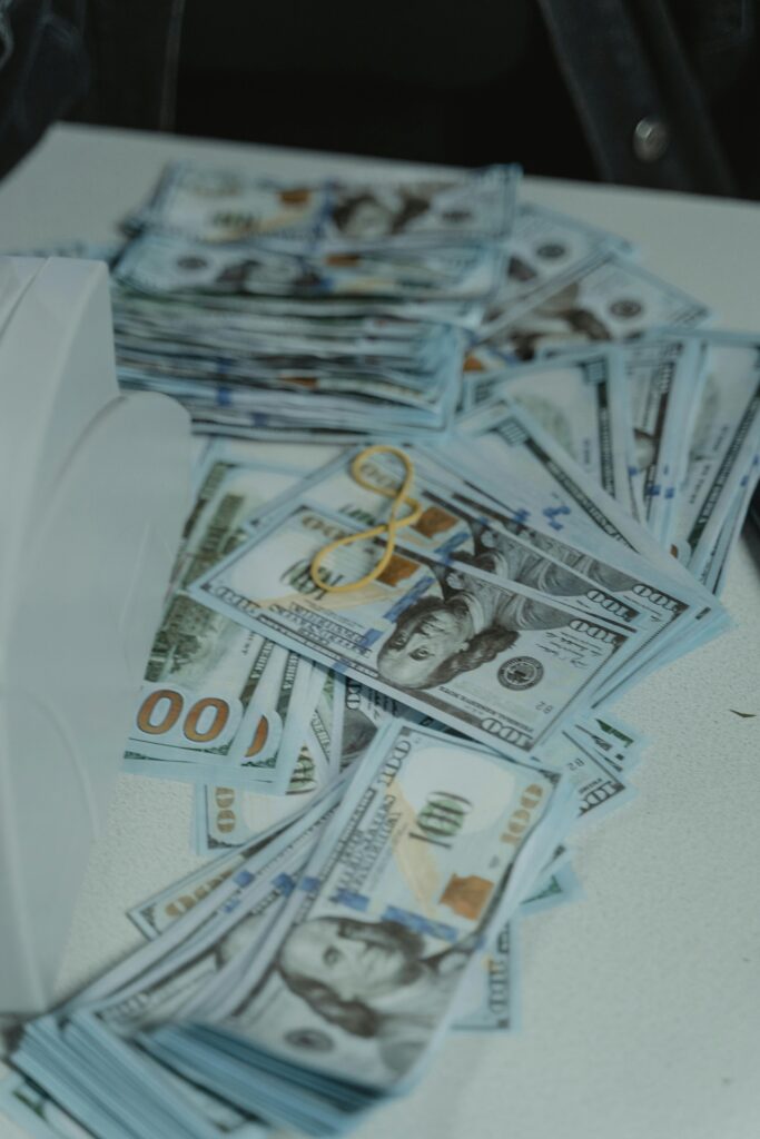 A pile of US dollar bills neatly stacked and secured with a rubber band on a white surface.